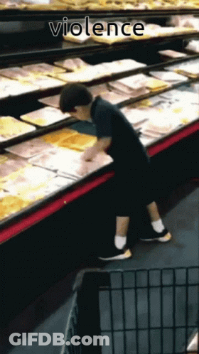 A Young Boy Reaches Into A Display Case In A Grocery Store With The Word Violence Below Him GIF