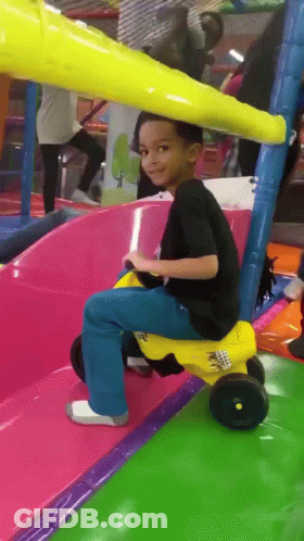 A Young Boy Riding A Yellow Toy Car On A Slide GIF