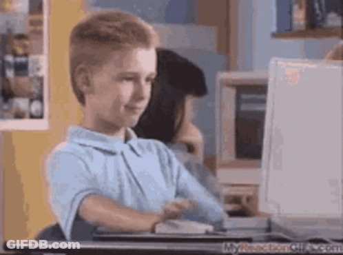 A Young Boy Sits At A Desk In Front Of A Computer GIF