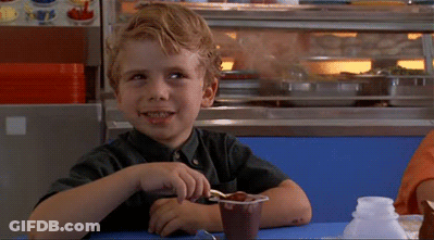 A Young Boy Sits At A Table With A Cup Of Chocolate Pudding GIF