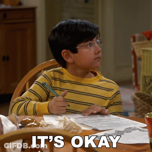 A Young Boy Sits At A Table With A Pen In His Hand And The Words " It 'S Okay " Written Below Him GIF