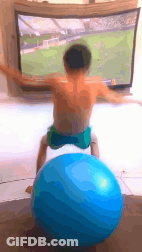 A Young Boy Sits On A Blue Exercise Ball In Front Of A Tv GIF