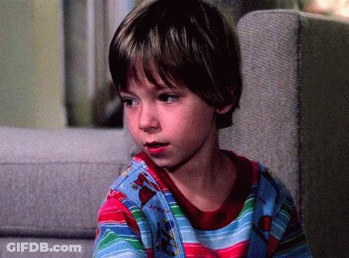 A Young Boy Sitting On A Couch Wearing A Striped Shirt With A Christmas Tree On It GIF