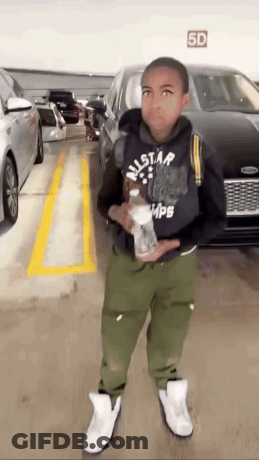 A Young Boy Standing In A Parking Lot With A 5D Sign Above Him GIF