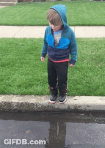 A Young Boy Standing In A Puddle With His Reflection In The Puddle GIF