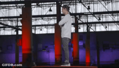 A Young Boy Stands On A Platform With His Arms Crossed In Front Of A Large Building GIF
