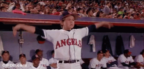 A Young Boy Wearing A Angels Baseball Uniform Is Standing In The Dugout With His Arms Outstretched . GIF