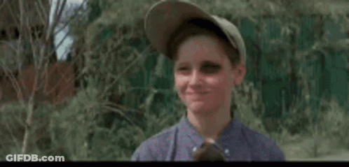 A Young Boy Wearing A Baseball Cap And A Blue Shirt Is Waving His Hand In The Air . GIF