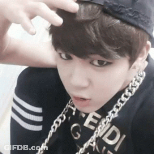 A Young Boy Wearing A Baseball Cap And A Chain Around His Neck Is Looking At The Camera . GIF