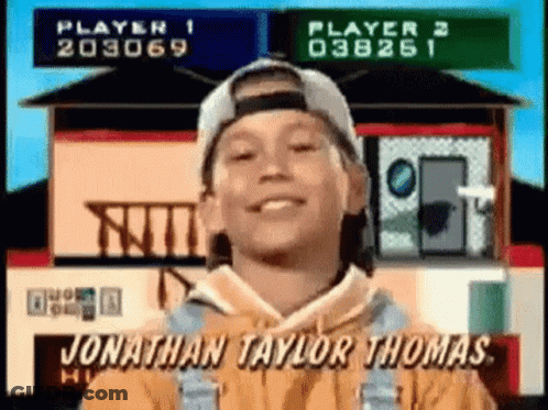 A Young Boy Wearing A Baseball Cap And Overalls Is Smiling In Front Of A House . GIF