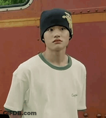A Young Boy Wearing A Beanie And A White T-Shirt Is Standing In Front Of A Red Truck . GIF
