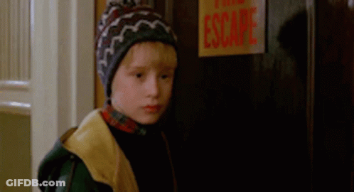 A Young Boy Wearing A Beanie Is Standing In Front Of A Door With A Sign That Says Escape . GIF