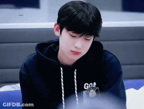 A Young Boy Wearing A Black Hoodie Is Sitting On A Couch . GIF