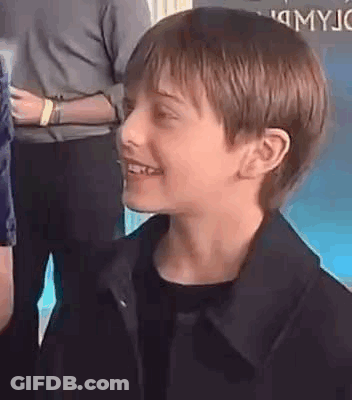 A Young Boy Wearing A Black Jacket Is Smiling And Looking At The Camera . GIF