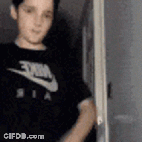 A Young Boy Wearing A Black Nike T-Shirt Is Standing In Front Of A Door . GIF