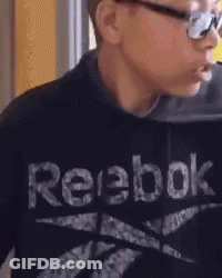 A Young Boy Wearing A Black Reebok Sweatshirt Is Eating Something . GIF
