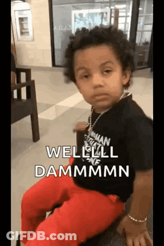 A Young Boy Wearing A Black Shirt And Red Pants Is Sitting On A Chair And Making A Funny Face . GIF