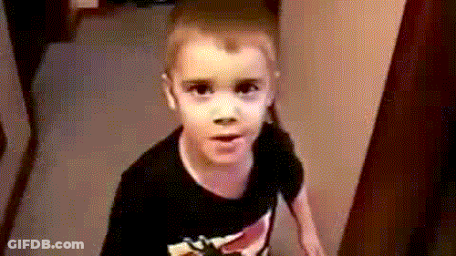 A Young Boy Wearing A Black Shirt Is Standing In A Hallway . GIF