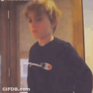 A Young Boy Wearing A Black Sweater Is Standing In Front Of A Door . GIF