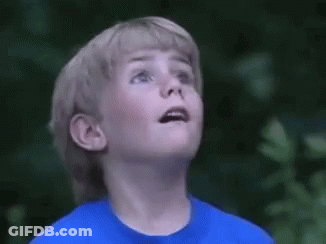 A Young Boy Wearing A Blue Shirt Is Looking Up At The Sky . GIF