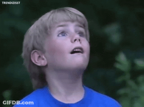 A Young Boy Wearing A Blue Shirt Is Looking Up At The Sky . GIF