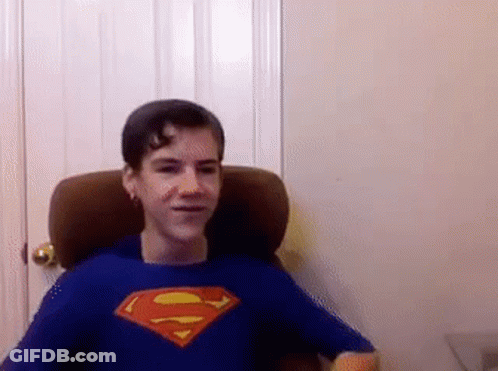 A Young Boy Wearing A Blue Superman Shirt Is Sitting In A Chair . GIF