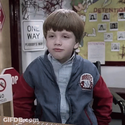 A Young Boy Wearing A Braves Jacket Is Sitting At A Desk In Front Of A One Way Sign . GIF