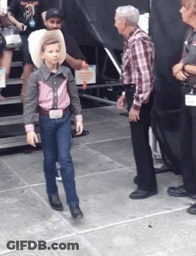 A Young Boy Wearing A Cowboy Hat And A Plaid Shirt Is Walking On A Stage GIF