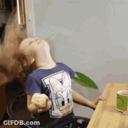A Young Boy Wearing A Donald Duck Shirt Is Sitting At A Table GIF