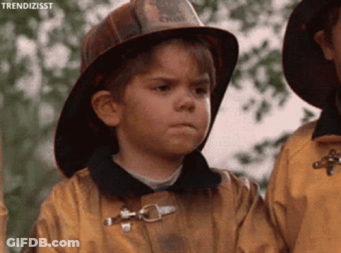 A Young Boy Wearing A Fireman 'S Hat And A Yellow Jacket GIF