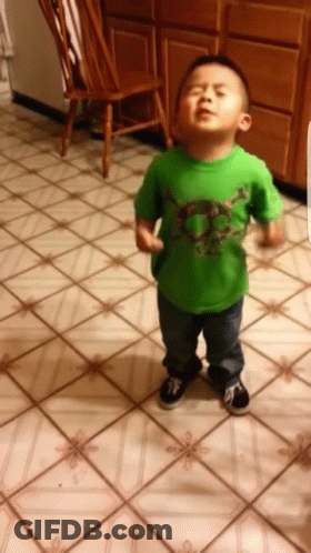 A Young Boy Wearing A Green Shirt With A Skull On It Stands On A Tiled Floor GIF