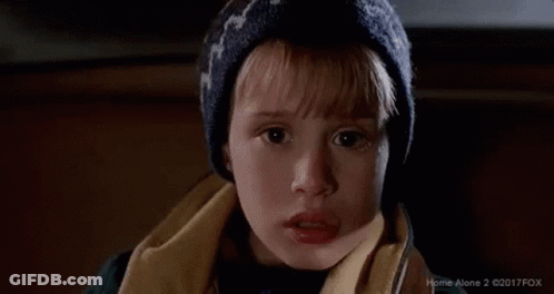A Young Boy Wearing A Hat And Scarf Is Looking At The Camera With A Surprised Look On His Face . GIF