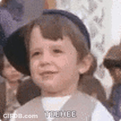 A Young Boy Wearing A Hat And Vest Is Making A Funny Face And Says Teehee . GIF