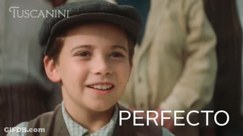 A Young Boy Wearing A Hat Is Smiling In Front Of A Tuscanini Ad GIF