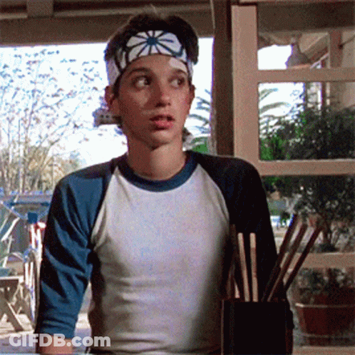 A Young Boy Wearing A Headband And A Baseball Shirt Is Holding Chopsticks GIF
