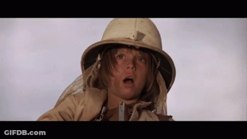 A Young Boy Wearing A Helmet And A Trench Coat Is Looking At The Camera . GIF