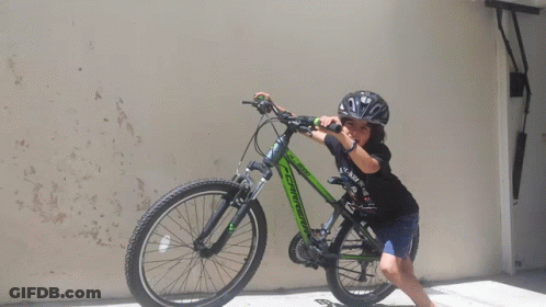 A Young Boy Wearing A Helmet Is Standing Next To A Green Bicycle GIF