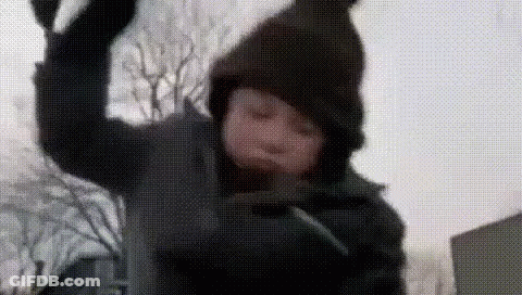 A Young Boy Wearing A Hooded Jacket And A Hat Is Throwing Snow In The Air . GIF