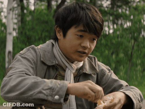 A Young Boy Wearing A Jacket And Scarf Is Eating A Piece Of Food GIF