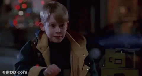 A Young Boy Wearing A Jacket Is Standing In Front Of A Christmas Tree And Smiling . GIF