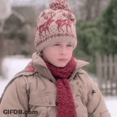 A Young Boy Wearing A Knitted Hat And Scarf Stands In The Snow GIF