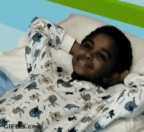 A Young Boy Wearing A Pajama Top With Dinosaurs On It Is Laying On A Bed GIF