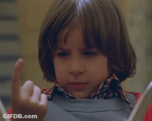 A Young Boy Wearing A Plaid Shirt And A Grey Sweater Looks At Something GIF
