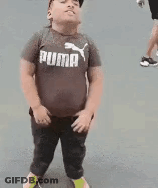 A Young Boy Wearing A Puma T-Shirt And A Hat Is Standing On A Sidewalk . GIF