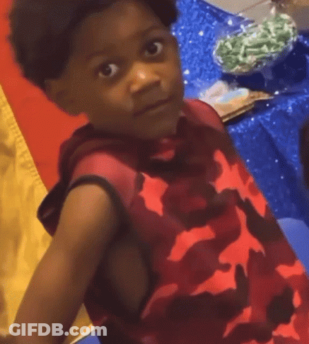 A Young Boy Wearing A Red Camo Shirt Is Looking At The Camera GIF