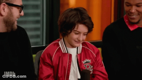 A Young Boy Wearing A Red Jacket With A Crown On It Is Talking Into A Microphone . GIF