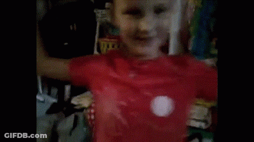 A Young Boy Wearing A Red Shirt Is Standing In Front Of A Shelf GIF