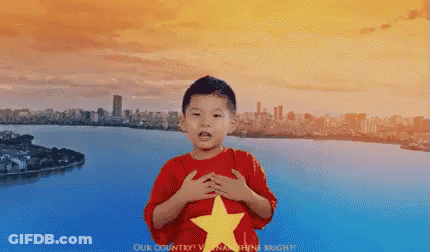 A Young Boy Wearing A Red Shirt With A Yellow Star On It Stands In Front Of A River GIF