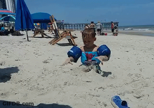 A Young Boy Wearing A Spiderman Shirt Is Playing In The Sand On The Beach GIF