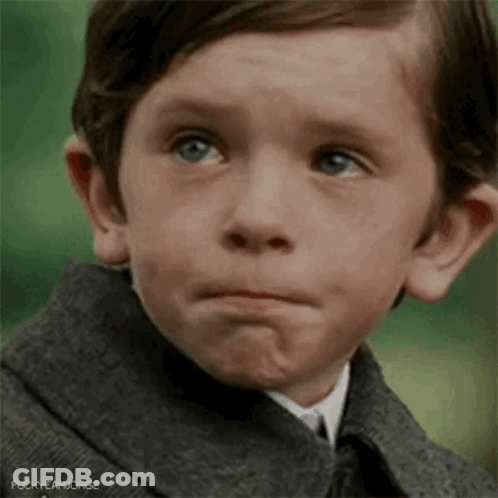 A Young Boy Wearing A Suit And Tie Is Making A Sad Face . GIF